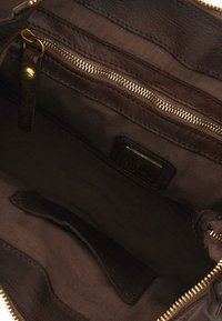 Interno di una borsa in pelle marrone con una tasca con cerniera, rivestimento in tessuto liscio e una tasca a fessura. Dettagli in metallo dorato visibili.