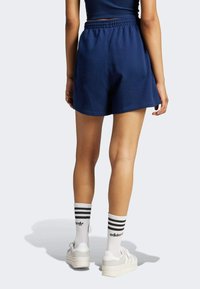 Mörkblå bomullsshorts med elastisk midja, i en avslappnad design och med slät textur, kombinerat med vita strumpor och skor.