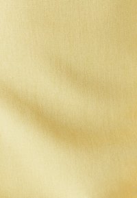 Heledal kollase värvusega tekstiilkangas, millel on sile tekstuur ja õrn koepat • niti muster. Puuduvad nähtavad mustrid või aksendid.