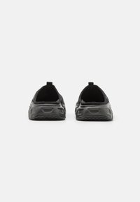 Pantofi sport negri cu un superior texturat, design elastic de tip slip-on și o talpă groasă din cauciuc cu un profil tipărit pentru aderență.