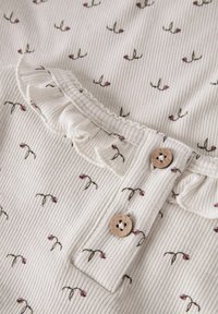 Ribbet hvidt stof top med lille blomstermønster; har en flæset halsudskæring og træknapper til lukning.