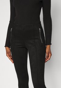 Svarta mockabyxor med slim fit, utrustade med dragkedjefickor på sidorna och en slät, texturerad yta.