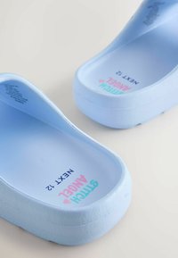 Saboti din cauciuc albastru deschis cu o suprafață texturată. Interiorul prezintă text imprimat: „Stitch Angel” și „Next 72” cu litere multicolore.