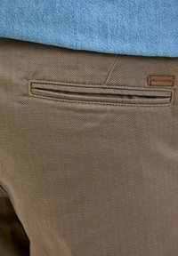 Brune bukser med en struktureret stof, der har en baglomme med en subtil horisontal åbning og et lille lædermærke, der står "JACK & JONES."