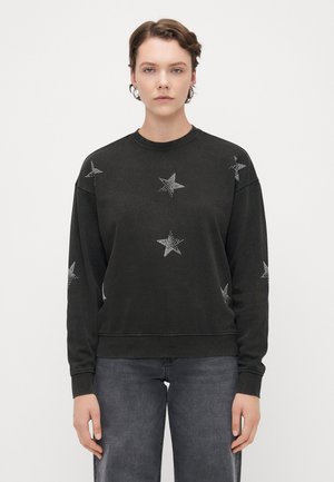 Svart hettegenser med lange ermer og sølvstjernedekorasjoner. Enkel mannsrund hals og ribbestrikkede mansjetter, kombinert med grå jeans.