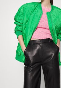 Groene gewatteerde bomberjack met geribbelde manchetten, gecombineerd met een textuur roze cropped trui en hoge zwarte leren broek.