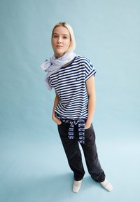 Striped blue and white t-shirt, relaxed fit, tied at the waist. Black pants, flat woven shoes. Soft texture, light background.