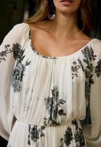 Leichtes, durchscheinendes Kleid mit schwarz- grauem Blumenmuster auf weißem Hintergrund. Verfügt über einen runden Ausschnitt und eine geraffte Taille.