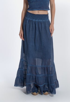 Donna che indossa una gonna lunga trasparente blu scuro a vita alta con orlo arricciato e scarpe espadrillas visibili.
