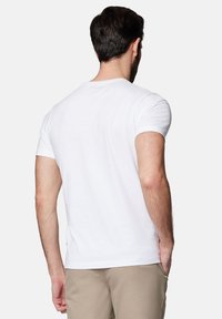 Biała bawełniana koszulka z krótkim rękawem, z okrągłym dekoltem i prostym dołem. Gładka tekstura z subtelnym logo blisko dekoltu.