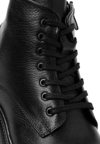 Bota de cuero negra con acabado texturizado, punta redonda y seis pares de ojales de metal con cordones negros. Detalles de costura a lo largo de la suela.