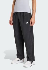 Schwarze Sporthose aus leichtem Stoff mit elastischem Bund, Seitentaschen und einem weißen Adidas-Logo auf dem linken Oberschenkel.