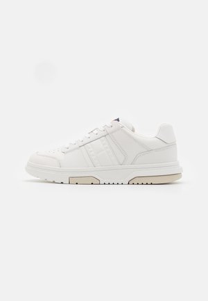 Low-top witte leren sneaker met veters, gevoerde kraag, subtiele gestikte strepen en een gestructureerde beige zool op een effen achtergrond.