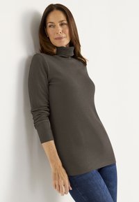 Dark brown turtleneck top with long sleeves, ribbed texture, and a relaxed fit, paired with blue jeans.