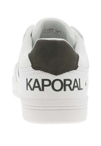 Baskets blanches avec un dessus en tissu texturé, talon en daim gris, et marquage "KAPORAL" à l'arrière. Semelle blanche plate, design minimaliste.