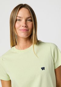T-shirt di cotone verde chiaro con scollo rotondo, maniche corte e un piccolo logo in navale sul lato sinistro del petto. Tessuto morbido.