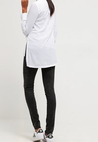 Vit långärmad skjorta med sidslitsar, i kombination med svarta slim-fit byxor och svartvita sneakers, vilket betonar en modern, avslappnad stil.