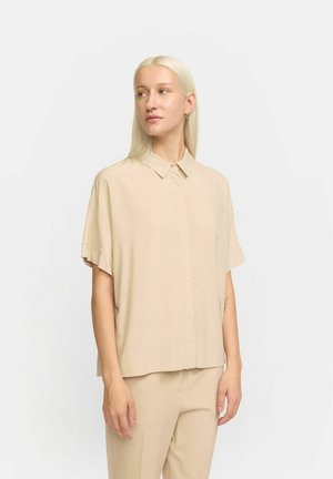 Beige short-sleeve shirt with a collar, featuring a button closure and smooth, lightweight fabric. Positioned neatly over matching trousers.