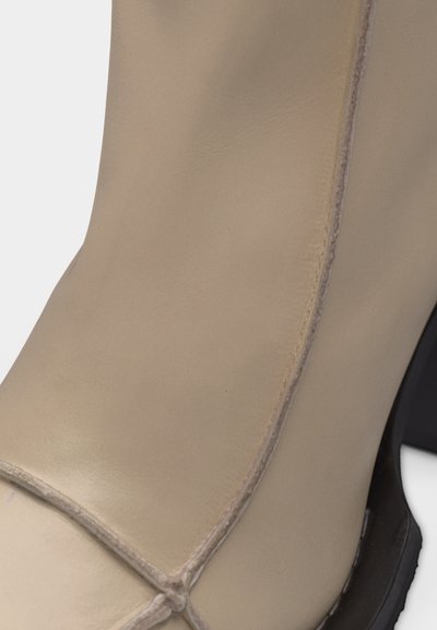 Μπεζ δερμάτινη μποτάκι αστραγάλου με εμφανείς ραφές και μαύρη σόλα.