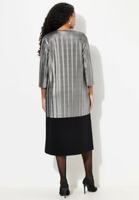 Grijze metallic gestreepte tuniek met driekwart mouwen, gecombineerd met een effen zwarte knielange rok. Zwarte hakken maken de look af.