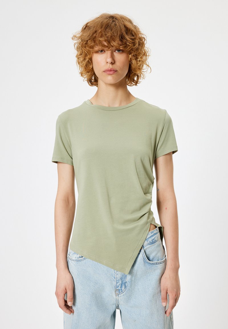 Kortærmet, lysegrøn t-shirt lavet af blødt stof. Har en asymmetrisk kant og en afslappet pasform. Matchet med lyseblå denimjeans.