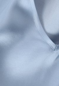Tissu en satin bleu clair avec une texture lisse ; présente un éclat subtil et un col rond avec des détails de couture précis.