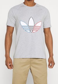 Grå kortärmad t-shirt med en stor flerfärgad Adidas trefoil-logotyp i blått, rött och svart kontur framtill.