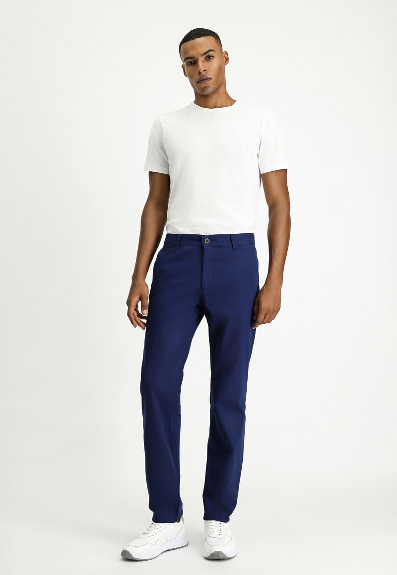 Pantalones azul marino de algodón con corte recto, que presentan un cierre con botón, pasadores para cinturón y una textura suave, combinados con una camiseta blanca.