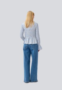 Top peplum azul e branco com padrão quadriculado e textura franzida, combinado com jeans de ganga azul de perna larga de cintura alta. Vista traseira, ajuste solto.