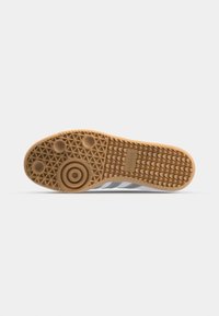Zool van een beige Adidas-schoen met cirkelvormige, driehoekige en golvende loopprofielen, met het Adidas-logo op het midden van de voet.
