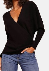 Maglione nero a costine con scollatura a V profonda, maniche lunghe morbide e vita aderente; abbinato a jeans blu.