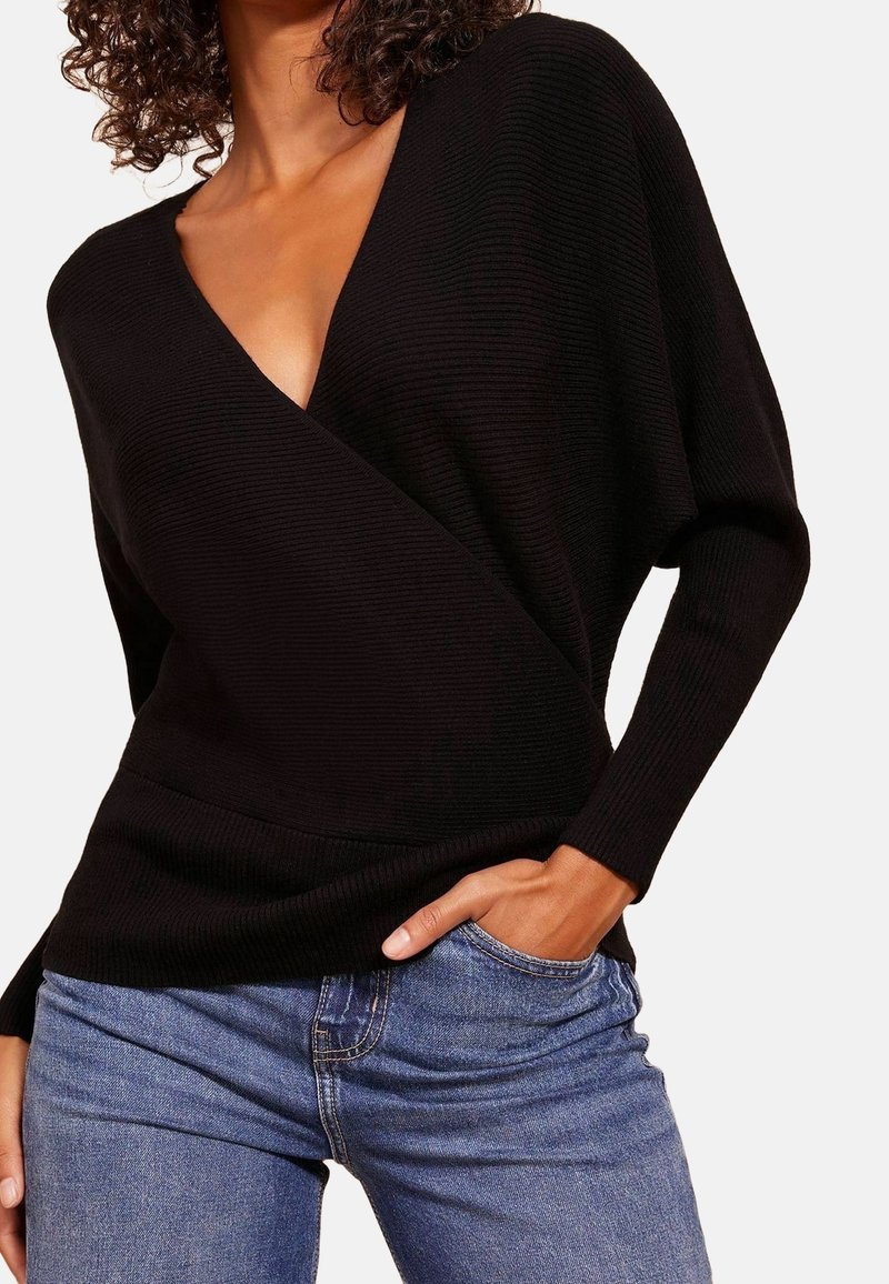 Maglione nero a costine con scollatura a V profonda, maniche lunghe morbide e vita aderente; abbinato a jeans blu.