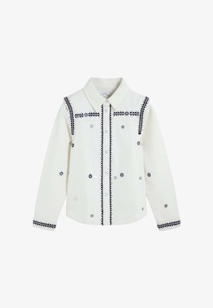 Chemise blanche à boutons avec broderie géométrique noire et rivets circulaires argentés sur le devant, les épaules, les manches et les poignets.