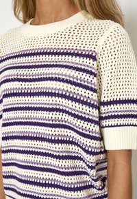 Suéter de punto de ganchillo en crema con rayas verticales en púrpura y lila. Mangas cortas, cuello redondo y textura de tejido abierto.