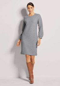 Graues Strickkleid mit rundem Ausschnitt und langen Puffärmeln, hat eine gerade Silhouette und einen gerippten Saum, kombiniert mit braunen kniehohen Stiefeln.