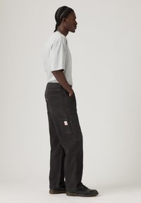 Μαύροι παντελόνια cargo με πολλές τσέπες, άνετη εφαρμογή και ορατές ραφές. Συνδυασμένα με ανοιχτό γκρι κοντομάνικη μπλούζα.