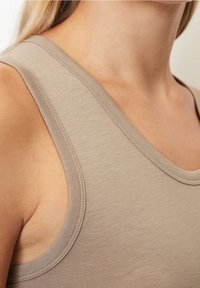 Top sin mangas de color beige con escote redondeado y tirantes anchos, hecho de una tela suave y ligera. Presenta costuras cuidadas a lo largo de los bordes.