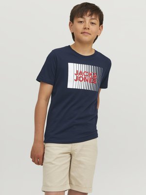 Námořnické modré bavlněné tričko s bílým a červeným logem "JACK & JONES", spárované se světlými krajkovými šortkami do půli stehen. Jednoduchý a neformální design.
