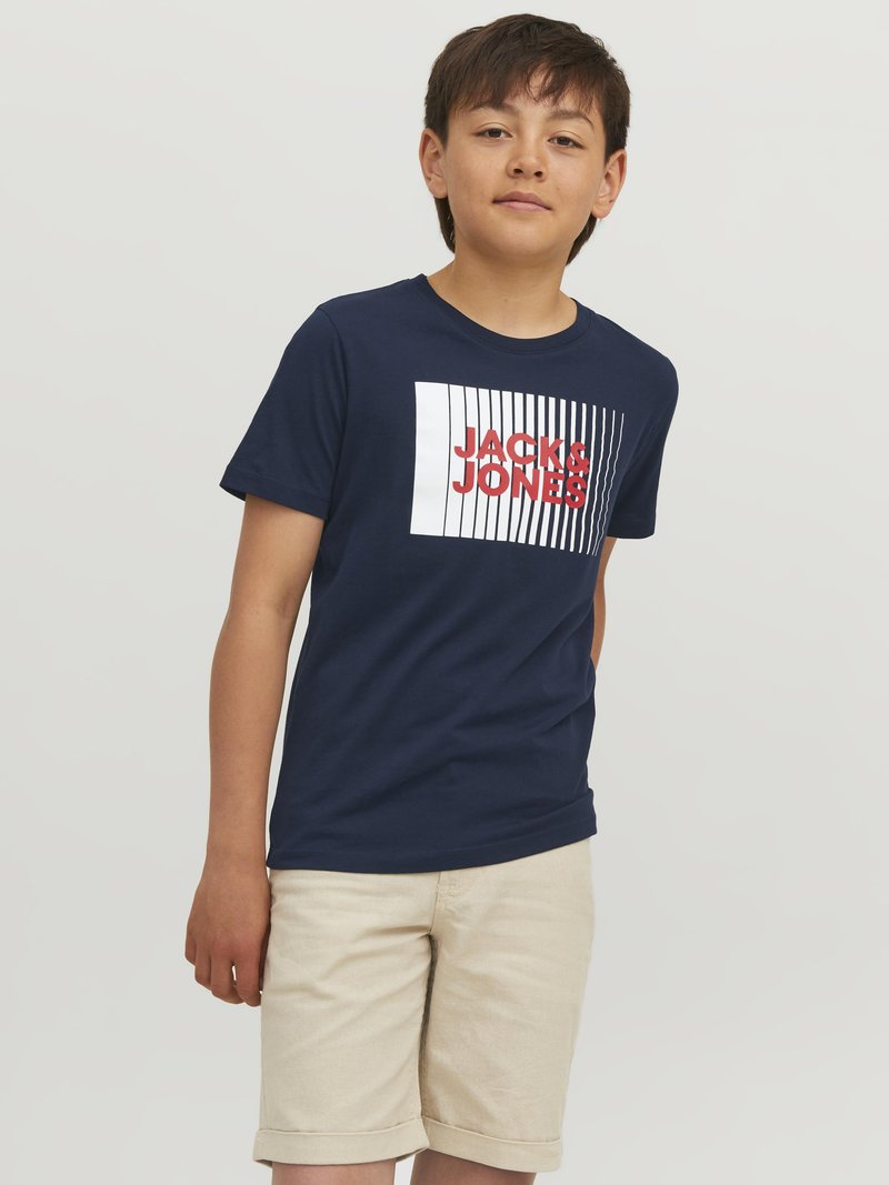 Námořnické modré bavlněné tričko s bílým a červeným logem "JACK & JONES", spárované se světlými krajkovými šortkami do půli stehen. Jednoduchý a neformální design.