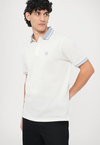 Hvit polotrøye med blåstripet krage og mansjetter, med korte ermer og en liten brodert logo på brystet.