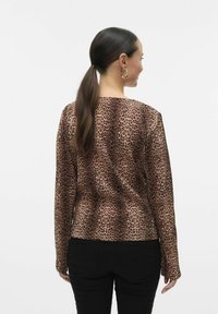 Duga majica sa leopard uzorkom, od prozirnog materijala s uskim krojem. Detalji uključuju okrugli izrez i crne hlače.