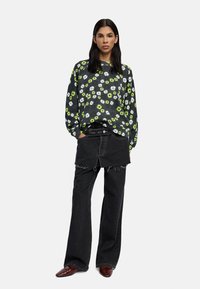  Czarna bluza z kwiatowym wzorem w intensywną zieleń i biel, połączona z zniszczonymi szerokimi spodniami w kolorze czarnym i brązowymi butami.