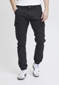 Sorte cargo-bukser med flere sidelommer, tætsiddende ankler, knaplukning og en letvægts, holdbar tekstur. Båret med sporty sneakers.