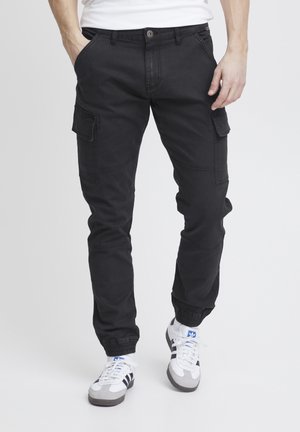 Svarta cargobyxor med flera sidsfickor, avsmalnande anklar, knäppning och ett lätt, hållbart tyg. Bärs med sportiga sneakers.