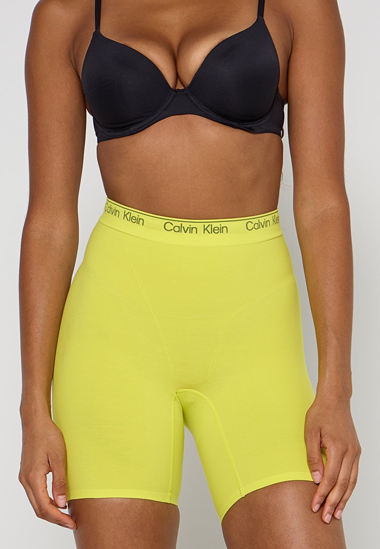 Spodenki do kolan z wysokim stanem w jaskrawym żółtym kolorze, wykonane z gładkiego, elastycznego materiału. Posiadają czarny pas z logo Calvin Klein.