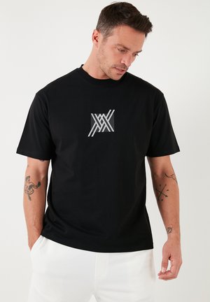 Zwarte katoenen t-shirt met een ronde halslijn, voorzien van een grijze geometrische grafiek op de borst. Korte mouwen en een relaxte pasvorm.