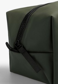 Bolsa de tela texturizada verde con cremallera y tirador negro, que presenta una forma geométrica y un cierre seguro. Las esquinas reforzadas mejoran la durabilidad.