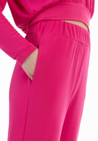 Heldere roze sportbroek met een gladde stof, elastische tailleband en zijzakken, die een gevormd en comfortabel ontwerp benadrukt.