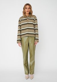 Polo shirt à rayures à manches longues en vert et marron terni, avec trois boutons. Associé à un pantalon vert olive brillant et des talons beiges.