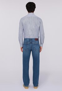 Jeans in denim blu con taglio dritto e cinque tasche, abbinati a una camicia a maniche lunghe a righe. L'outfit presenta un'etichetta in pelle marrone in vita.